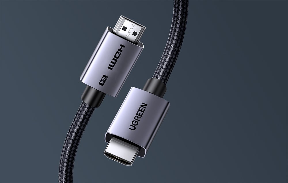 Zbliżenie na dwie metalowe końcówki kabla HDMI z czarnym oplotem na jednolitym, szarym tle