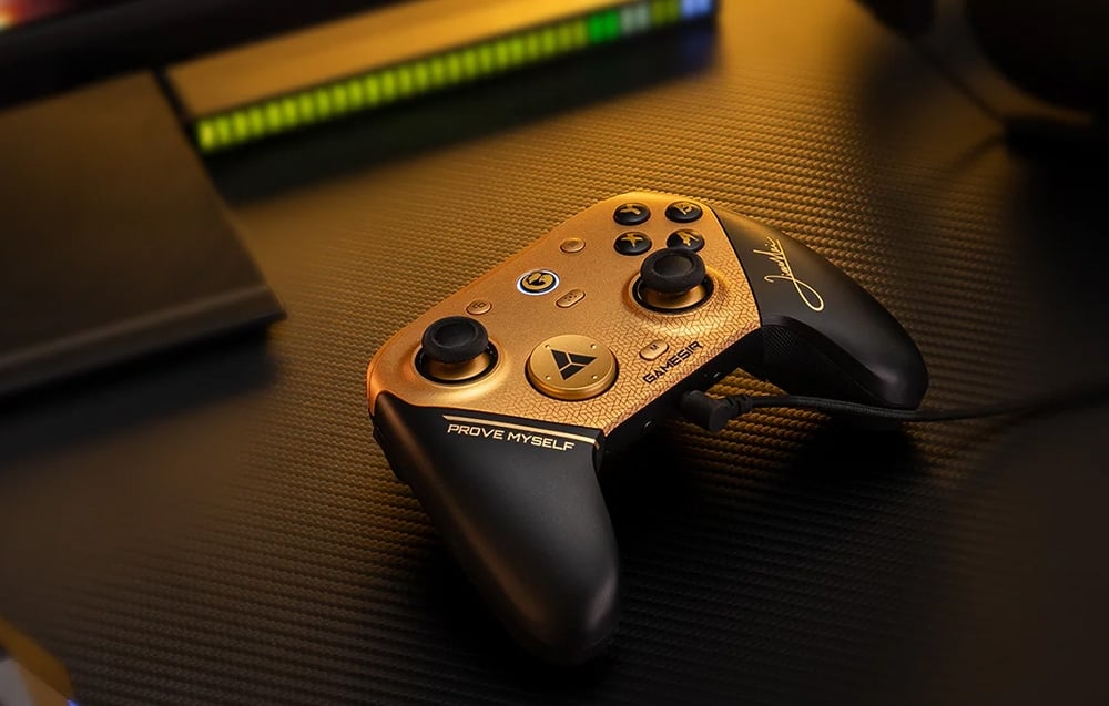 Black-gold game controller connected via USB lying on a desk with backlighting in the background