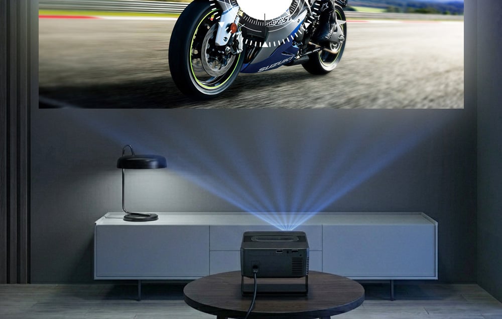 A projektor egy asztalon áll, és egy motorkerékpár képét vetíti a nagy képernyőre egy modern belső térben.