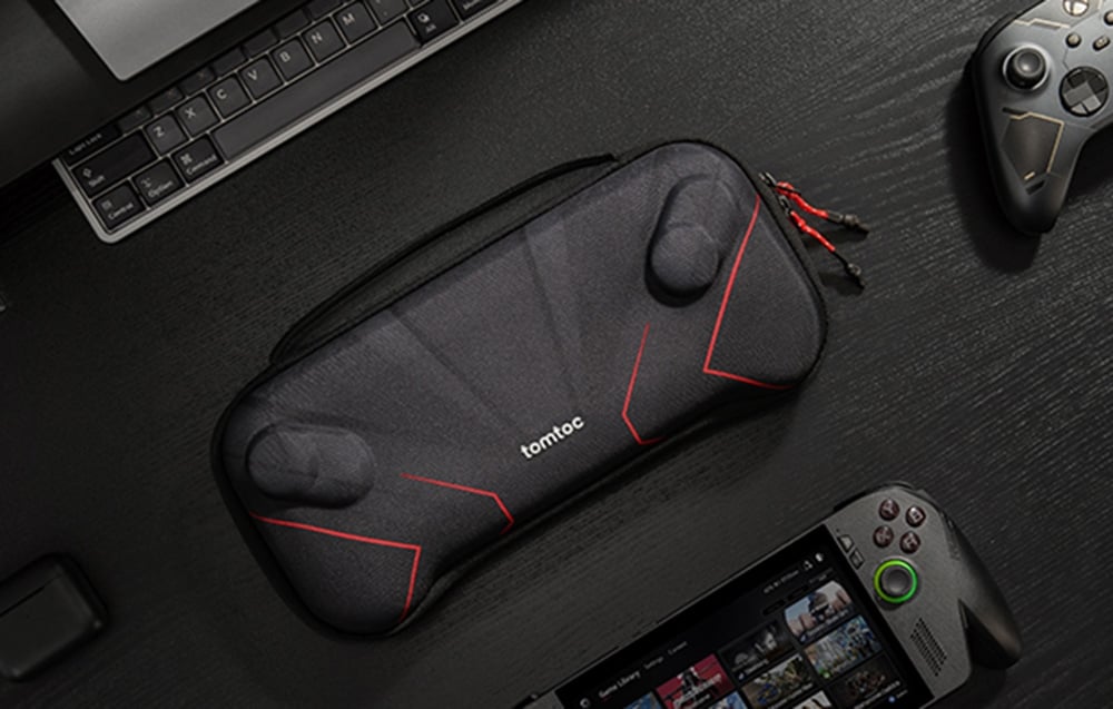 Closed black case by tomtoc with red accents lying on a dark desk next to a console and controller.
