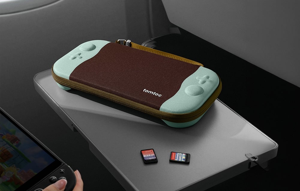 Zamknięte etui tomtoc leży na stoliku w samolocie obok dwóch kart z grami oraz fragmentu konsoli.