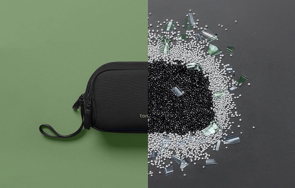 Czarne etui na akcesoria tomtoc na zielonym tle obok granulatu i fragmentów plastiku z recyklingu.