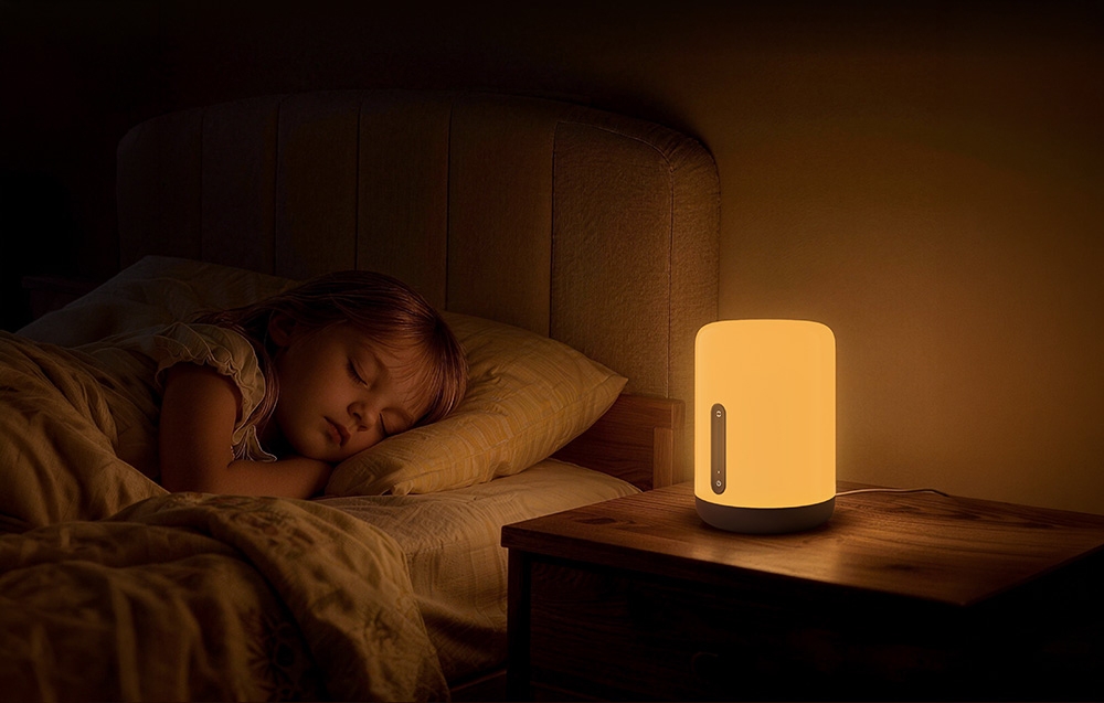 Child sleeping in bed, next to which a lamp shines with warm light on a wooden nightstand