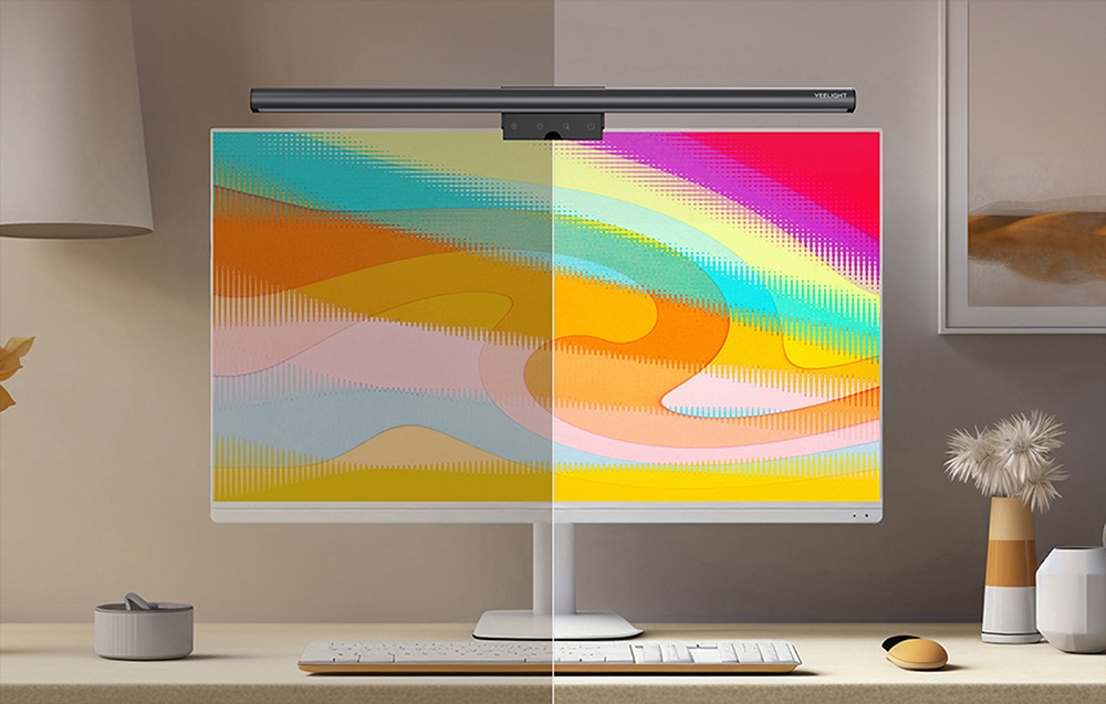 Monitor with Yeelight lamp on a bright desk with flowers and a mouse, the screen displays a colorful, split image
