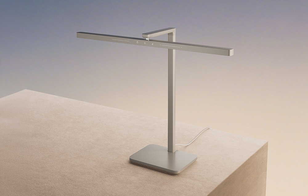 Lampă de birou LED modernă, argintie, cu un design minimalist, așezată pe o bază bej