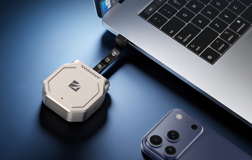 Srebrny adapter do dysków Freewell podłączony elastycznym kablem USB-C do laptopa obok leżącego smartfona