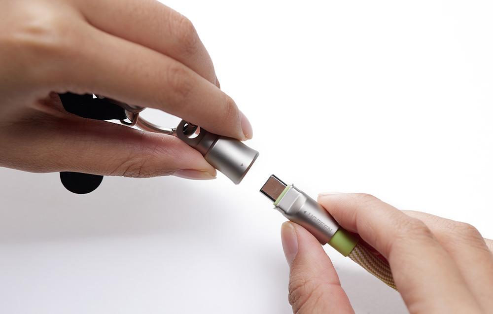 Dwie dłonie łączące wtyczkę USB-C kabla Ugreen z metalową nasadką breloka
