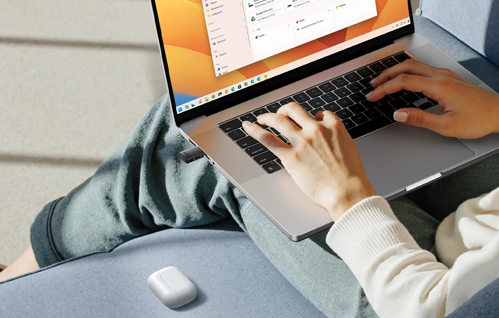 Osoba pisząca na klawiaturze laptopa z wpiętym adapterem USB-C, obok leżą słuchawki bezprzewodowe
