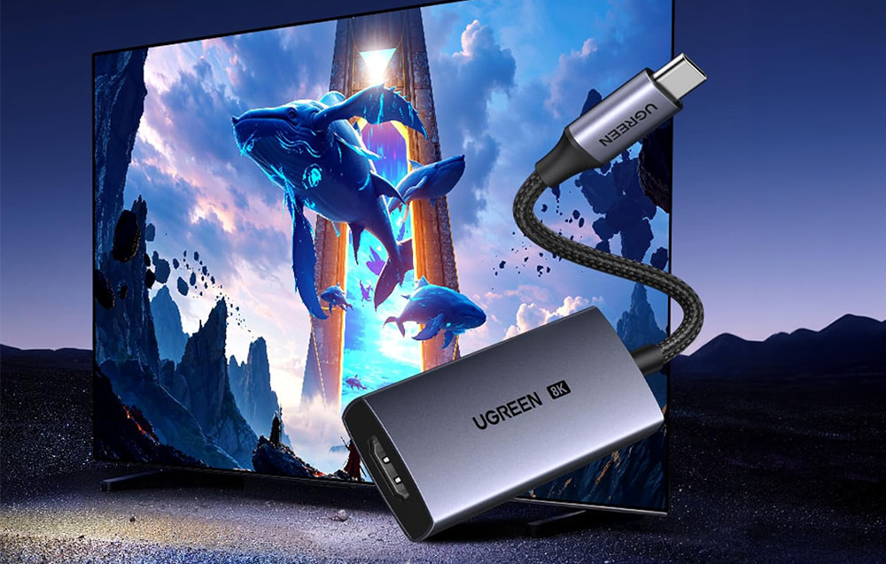 Szary adapter Ugreen 8K na tle wielkiego ekranu wyświetlającego grafikę z wielorybami
