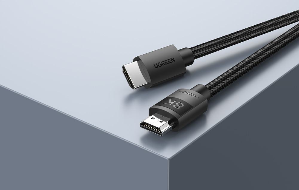 Czarny kabel HDMI w oplocie marki Ugreen z oznaczeniem 8K leżący na szarym podłożu.