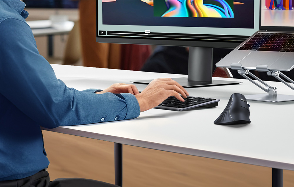 A person typing on a keyboard at a desk next to a vertical computer mouse and monitor