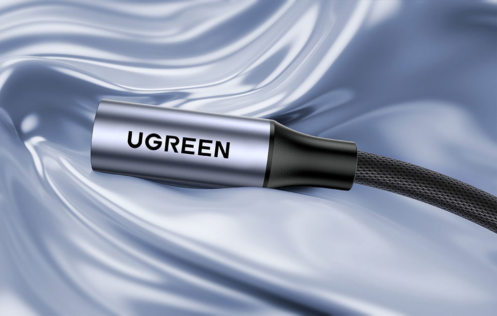 Zbliżenie na aluminiową wtyczkę adaptera audio marki UGREEN na pofalowanym, błyszczącym tle