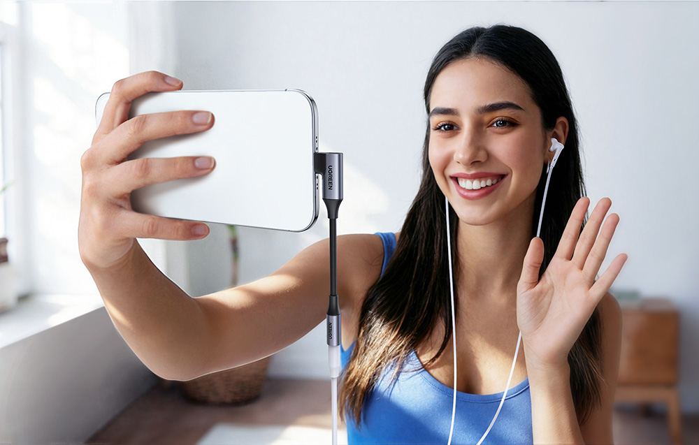 Uśmiechnięta kobieta robi selfie telefonem z podłączonym adapterem audio i słuchawkami