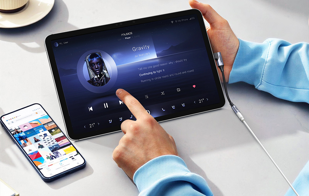 Dłoń obsługująca aplikację muzyczną na tablecie połączonym adapterem audio z przewodem