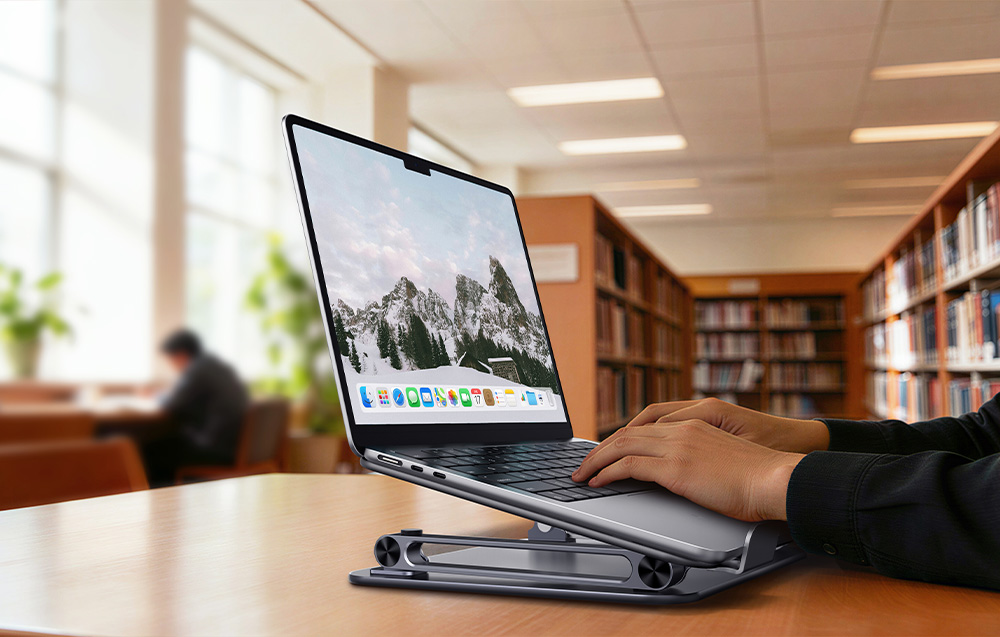 Dłonie piszące na laptopie opartym na złożonej, aluminiowej podstawce w bibliotece