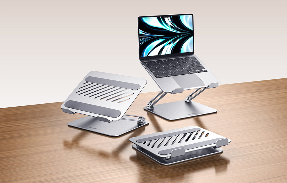 Trzy metalowe podstawki pod laptop – jedna z laptopem, dwie puste na drewnianym blacie