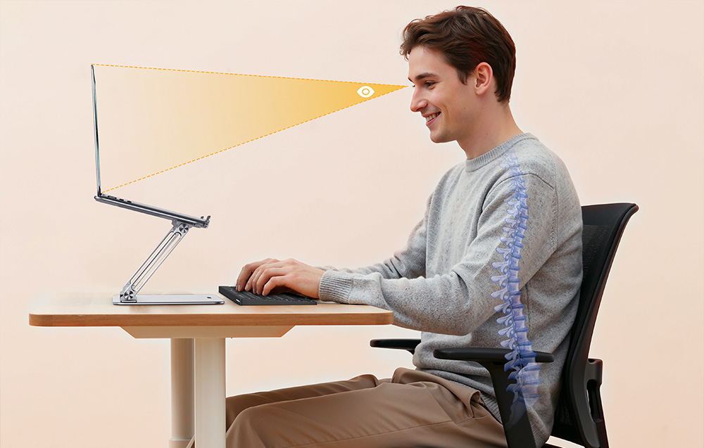 Mężczyzna siedzący przy biurku i patrzący na laptopa umieszczonego na regulowanej podstawce