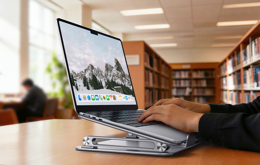 Dłonie piszące na laptopie opartym na złożonej, aluminiowej podstawce w bibliotece