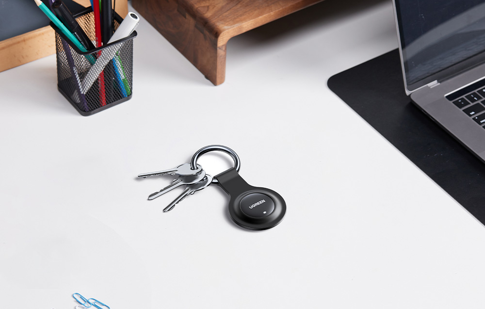 Black Ugreen locator attached to keys lying on a white desk next to a laptop