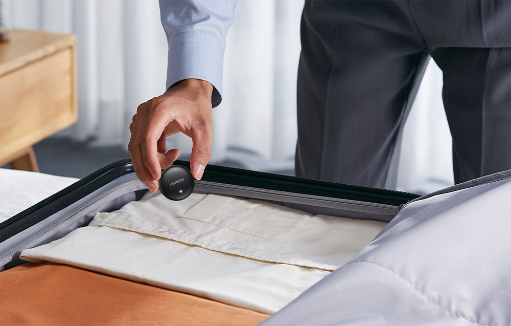 Man in a suit putting a black Ugreen locator into an open suitcase with clothes