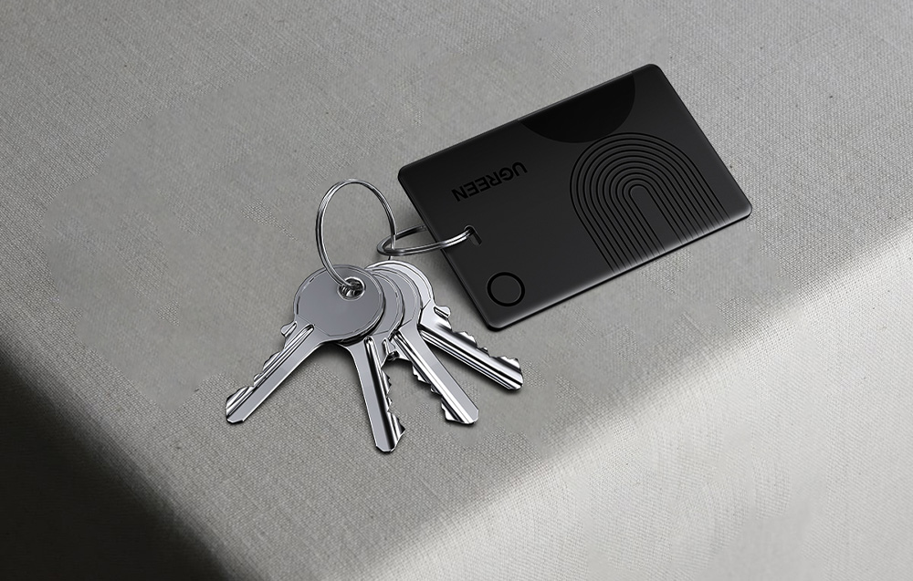 Black Ugreen card locator attached to a bunch of keys lying on a light fabric