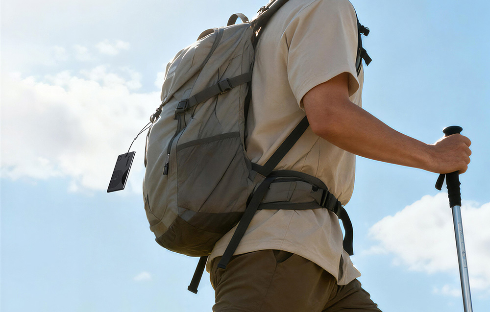 Man with a backpack and trekking pole with a black Ugreen locator attached
