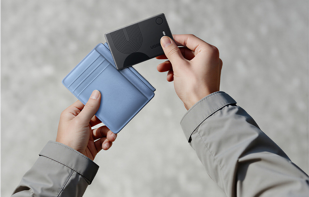 Hands placing the black Ugreen card locator into a blue wallet
