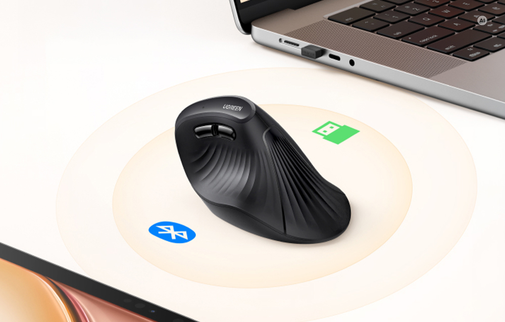 Mouse-ul vertical negru Ugreen stând pe un fundal deschis lângă un laptop cu pictogramele Bluetooth și USB vizibile