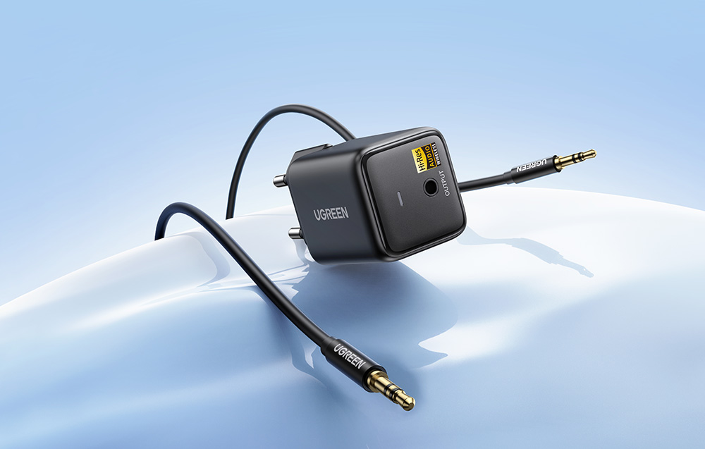 Czarny nadajnik audio Ugreen z podłączonym przewodem ze złoconymi wtykami mini jack na jasnym tle