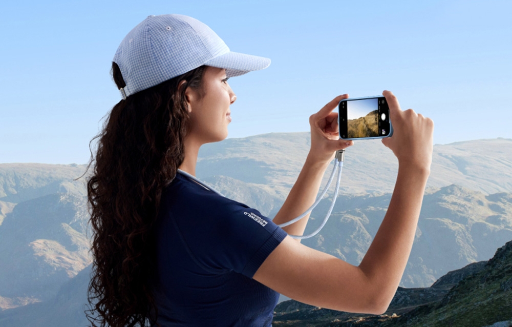 Woman in a hat taking a photo with a smartphone on a Ugreen lanyard in the mountains