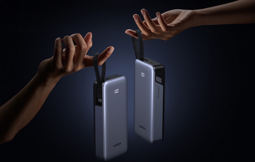 Two hands holding two gray Ugreen power banks by their built-in straps with LED displays