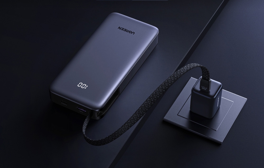 Gray Ugreen power bank with a digital display charging from a wall socket using the built-in cable
