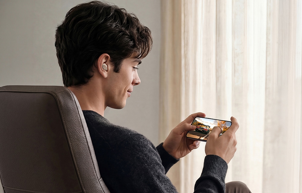 A boy in wireless headphones watching a movie on a smartphone while sitting in a chair in a room