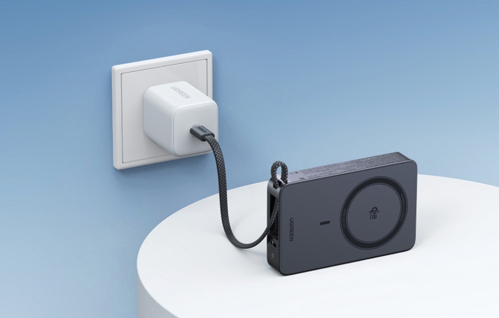 Gray Ugreen wireless power bank standing on a white table and connected to a charger via cable