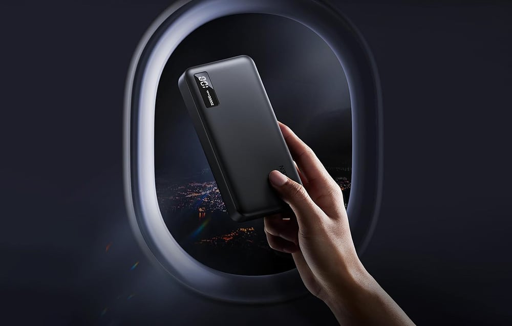 A hand holding a black power bank against the backdrop of a round airplane window