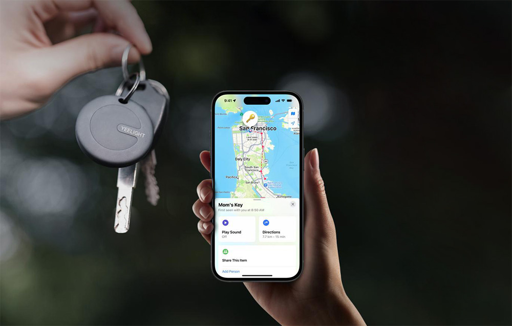 Lokalizator YEELIGHT przypięty do kluczy trzymanych w ręce obok smartfona z aplikacją lokalizacyjną pokazującą ich pozycję